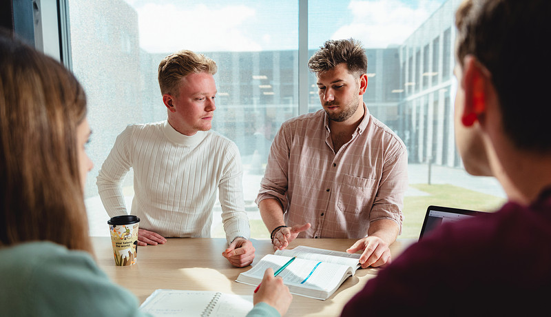 Students standing at table discussing open study book