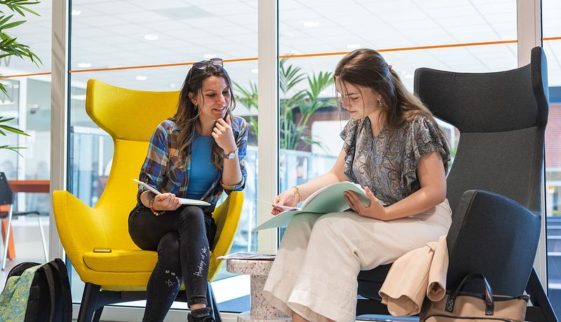 Two students sitting in comfy chairs looking at folder