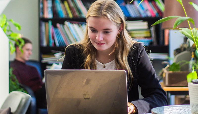 Student achter laptop met boekenkast 2022