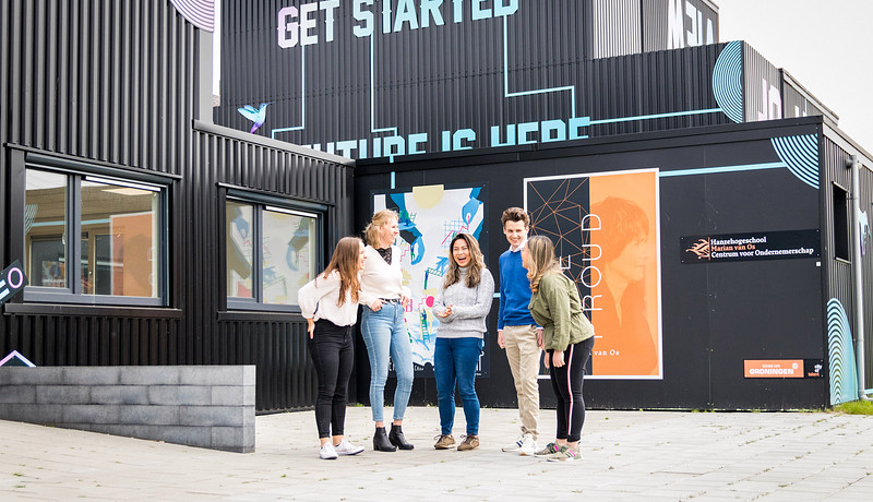 Five students standing outside in fron of container buildings with text 'get started'