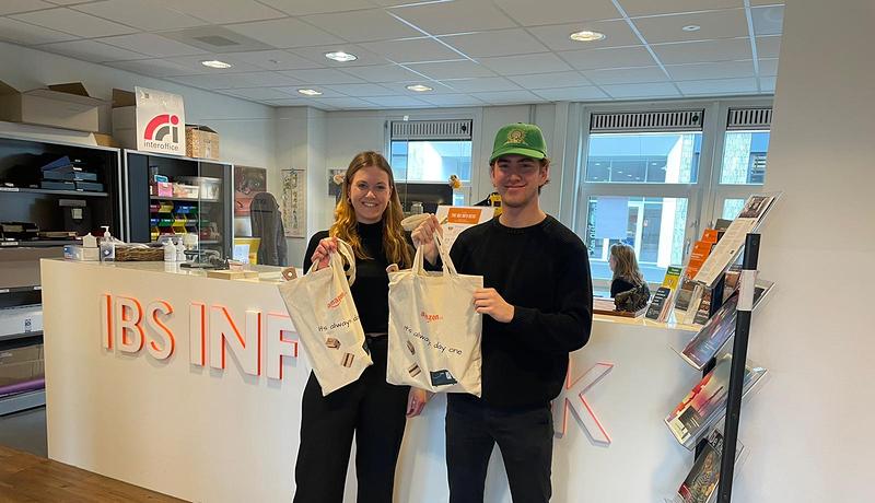 Two IBS students holding Amazon tote bag in front of IBS Info Desk