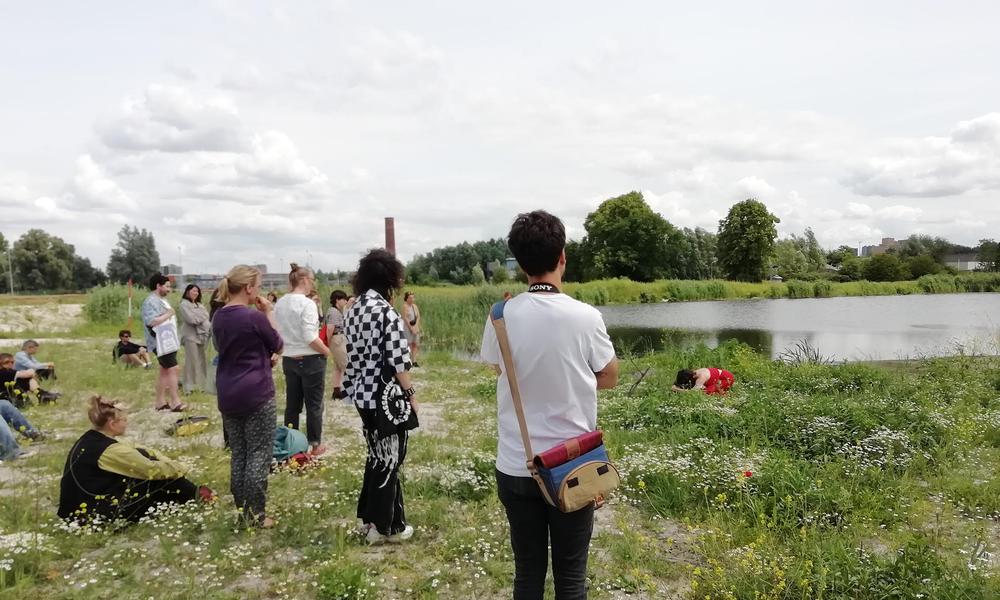 Een groep studenten staat in een grasveld te kijken naar een performance van een danser.