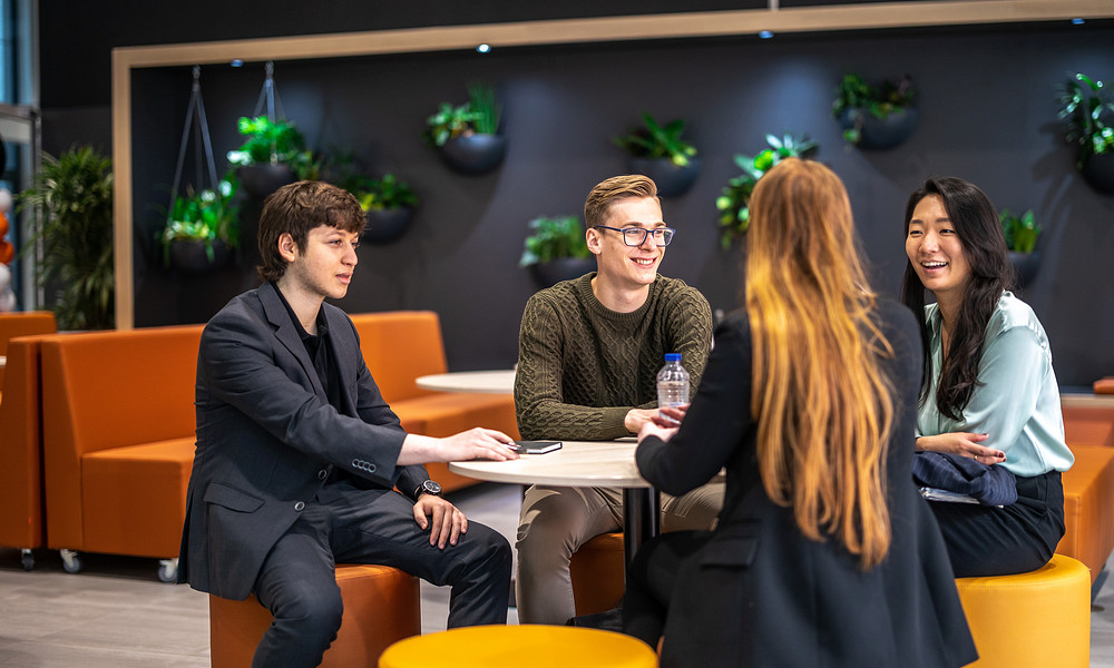 Four students sitting at round table, talking and laughing.