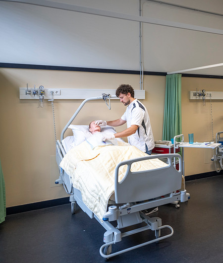 Verpleegkundige doet handeling bij oefenpop in verpleegbed