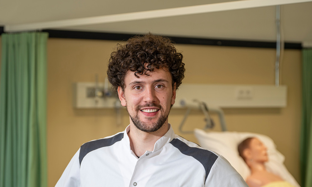 Jonge man met krullen kijkt lachend camera in heeft handen in zij