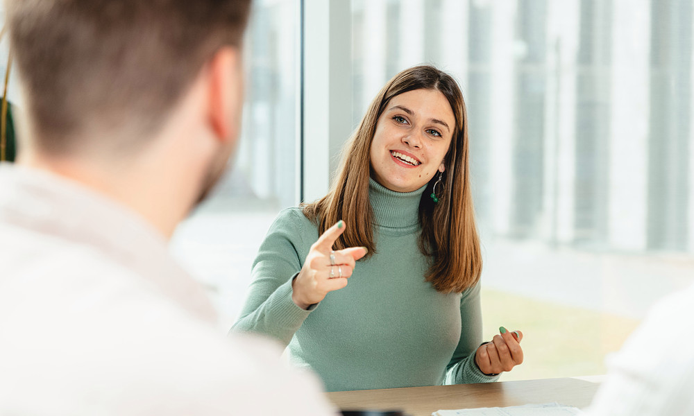 Student sitting at table explaining something to other student, using hands.