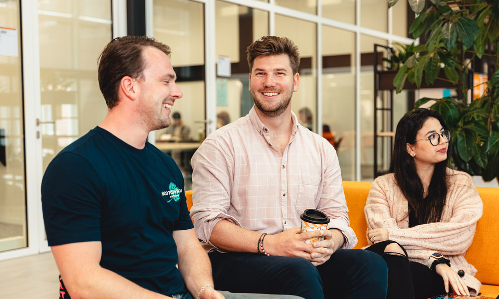 MSc in Business Studies student Nick sitting with two students, looking into camera