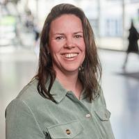 Nora Winters wearing a green button-up, standing in the main hall at Saxion, Enschede.