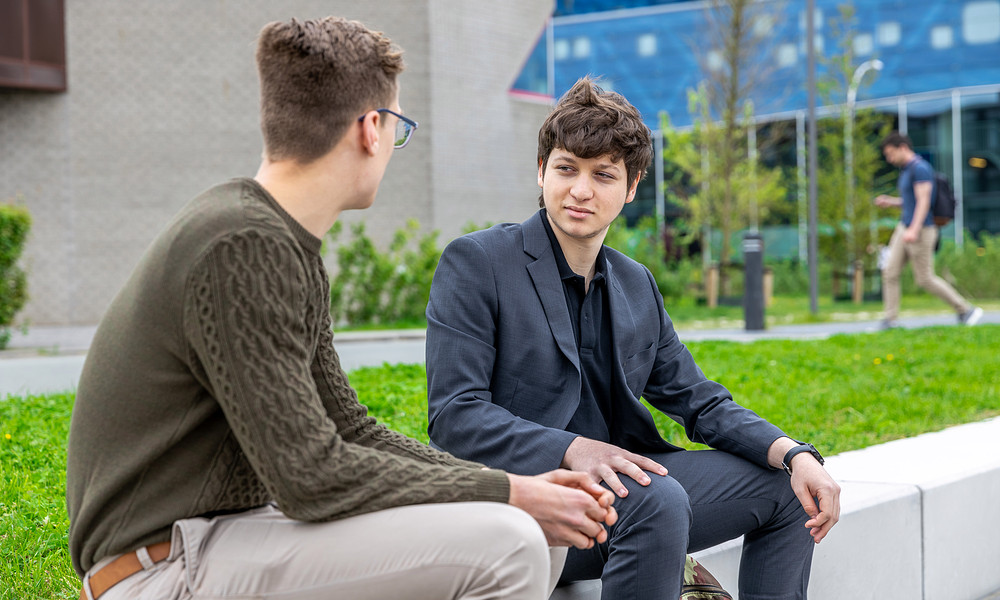 Two students sitting outside talking to each other