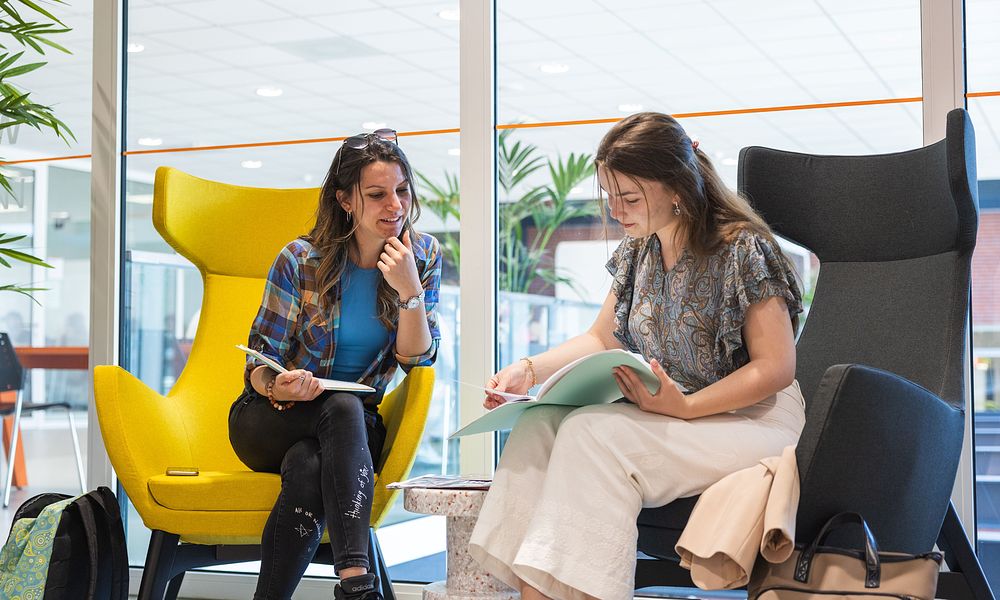 Two students sitting in comfy chairs looking at folder