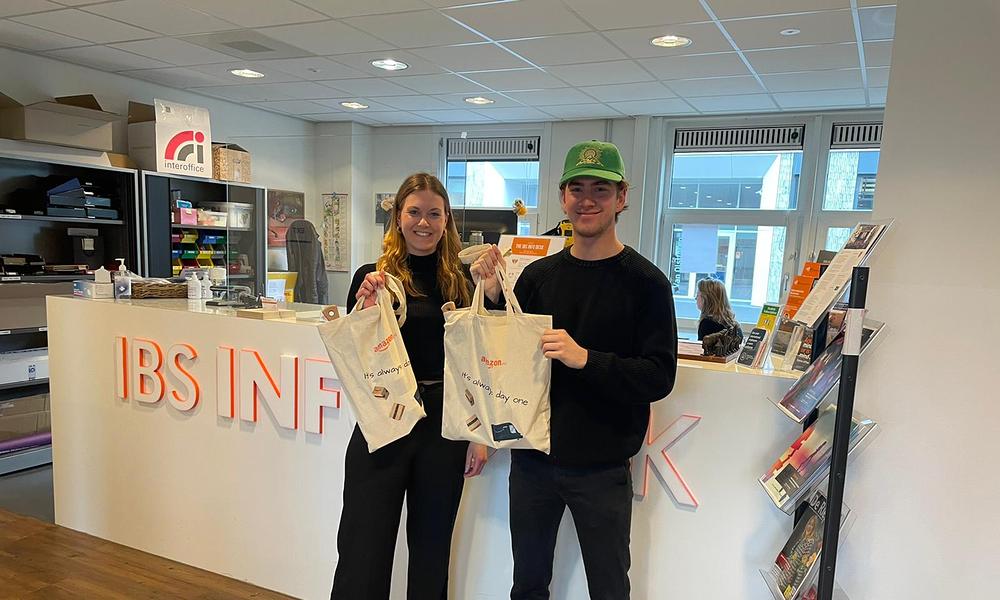 Two IBS students holding Amazon tote bag in front of IBS Info Desk