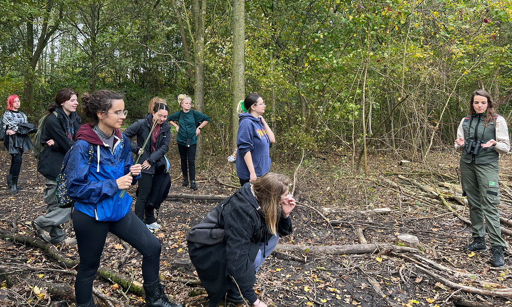 Een groep studenten staan in een bos te luisteren naar iemand die ze iets vertelt