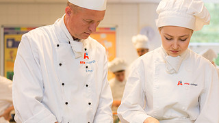 Kok, docent en student in kokskleding werken samen in de keuken